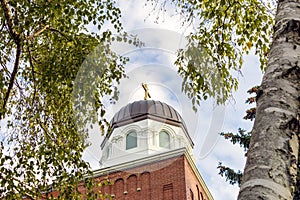 View from behind birch trees on a red brick building of an old Russian Orthodox church