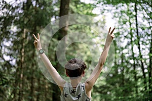 View from behind of a boy in his eary teens standing with his arms raised high in victorious gesture