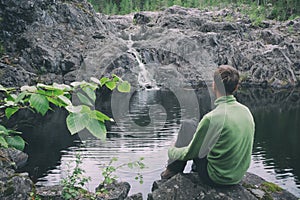 View from behind man hiker traveller sitting near mountain waterfall. Peaceful and calmness scenic view. Active person outdoor