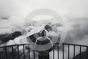 View from behind of a man standing at view point looking to beautiful landscape with foggy mountains in the distance. Black and