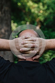 View from behind of mature man with little hair or alopecia with his hands on the nape of his neck.