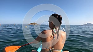 View from behind of a woman sitting on a stand up paddle board paddling towards a small island