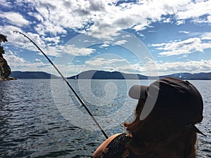 A view from behind of a young beautiful woman holding a fishing rod fishing in the ocean on a small boat in the gulf islands