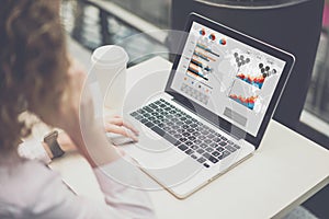 View from behind,young businesswoman sitting at desk and talking on phone,while using laptop with charts, graphs