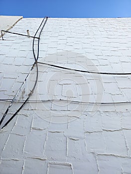 View from below of cement wall with black wiring and exterior pipes under blue sky. Architecture and construction