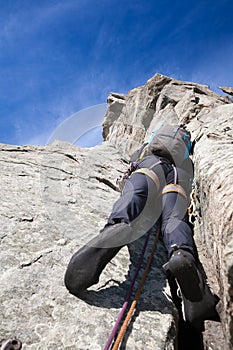 View from below of a climber while climbing a steep rock wall