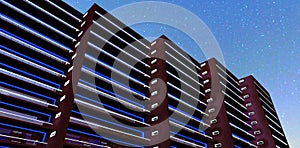 View from below of a magnificent apartment building at night. Blue straight lines of illumination. Sunset reflection. 3D rendering
