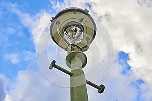 View from below of an old Berlin street lamp in front of a blue and cloudy sky