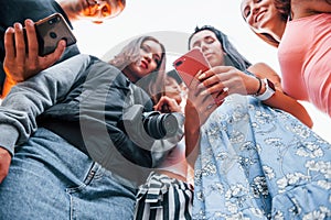 View from below. With phone. Group of young cheerful friends having fun together. Party outdoors