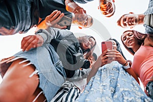 View from below. With phone. Group of young cheerful friends having fun together. Party outdoors