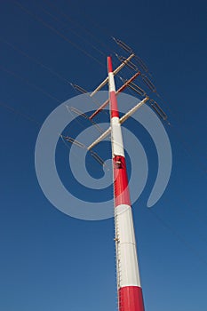 View from below of a red and white high voltage tower with blue sky as background