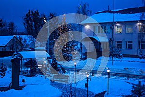 View of bench against christmas tree and shining lantern through snowing. Blue tone. Night shot.