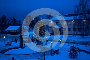 View of bench against christmas tree and shining lantern through snowing. Blue tone. Night shot.