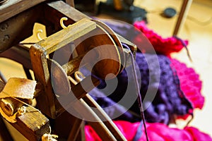 View beyond flyer of wooden old retro spinning wheel on knitted colorful purple pink blanket, ball of raw merino wool