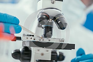 View of biochemist looking holding small stone with tweezers near microscope