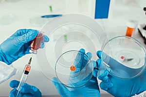 View of biochemist taking medicine with syringe near colleague holding petri dishes with biomaterial