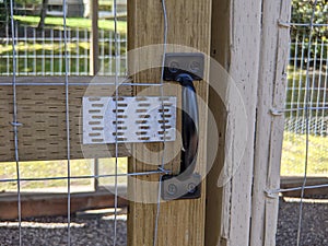 View of a black door handle on a chicken coup on a large farmland