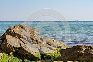 View of the Black Sea on a clear sunny day. On the shore, stones and sand, ships on the horizon. Blue sky and beautiful clouds