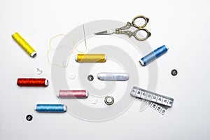 View of black and white buttons, needle with threaded yellow thread, various colors on spools of thread on white background and