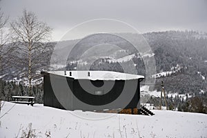 View of Black wooden tiny cabin with view on snowy pine forests in Ukraine