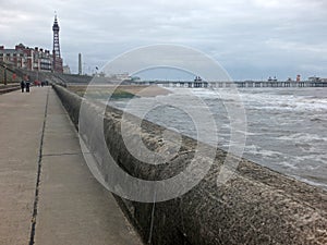 view of blackpool promenade in winter with stormy sea tower and central pier with unidentifiable people walking along the