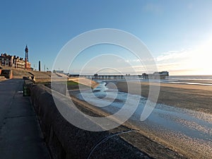 View of blackpool tower and north pier from the promenade with town buildings in afternoon sunlight