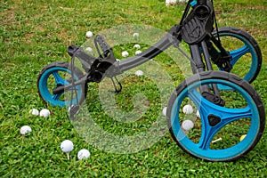 View of blue and black golf cart with three wheels, and white golf balls, on grass
