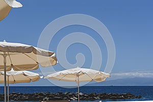 View of the blue sky at a beach on a sunny day with parasols for shade.