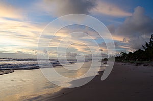 View of the blue sky and full of morning clouds on a beach with sea water reaching in the sand.