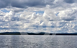 View of the blue sky over the lake with beautiful feathery and cumulonimbus clouds on a Sunny day, far away you can see