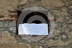 View of blue sky through square window of loophole in wall of an ancient fortress. Copy space photo