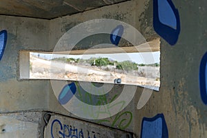 View of the border dividing strip through the embrasure in the concrete security separation fence on the border between Israel and