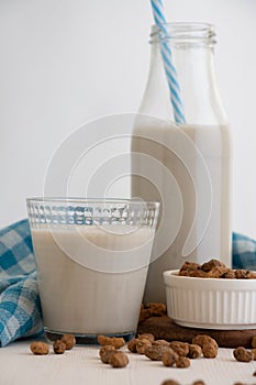 View of bottle with blue straw and glass with horchata and tiger nuts on white table