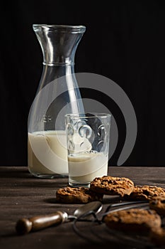 View of bottle and glass of milk on wooden table with chocolate chip cookie, selective focus, black background, vertical