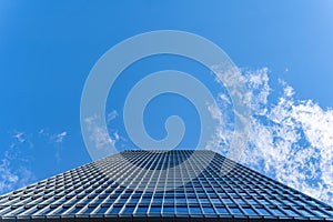 View from the bottom of office tower skycrapper building with glass windows in cloud blue sky