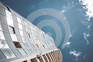 View from the bottom of office tower skycrapper building with glass windows in cloud blue sky