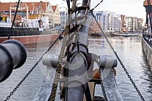 View from the bow of an old sailing ship with ropes and chains, overlooking a historic city waterfront.