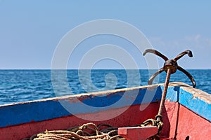 View of the bow of an old wooden boat sailing. Metal anchor, sea or ocean under clear sky