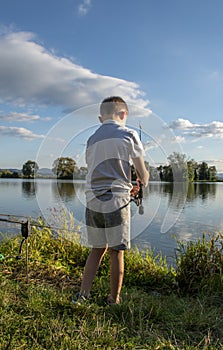 View on boy fishing on a lake from behind. Beautiful fish pond in Badin, near Banska Bystrica, Slovakia. Child holding fishing rod