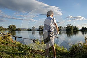 View on boy fishing on a lake from behind. Beautiful fish pond in Badin, near Banska Bystrica, Slovakia. Child holding fishing rod