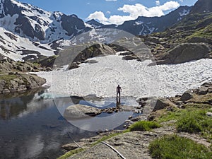 View from Bremer Hutte on man hiker standing in lake from melting snow tongues and snow-capped moutain peaks, lush green photo