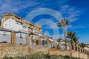 View of a brick wall with metal fence and palm trees with white houses