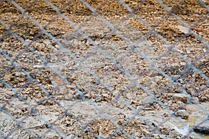 View of the brown earth through a metal wicker iron grid netting net. The background. Texture