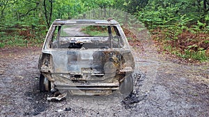 View burnt out and rusty car wreck alongside road and woods