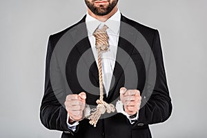 View of businessman in black suit and handcuffs with noose on neck isolated on grey