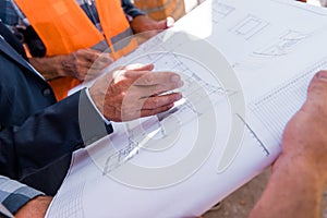 View of businessman gesturing near blueprint and constructors