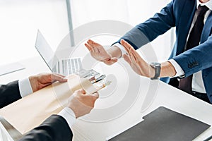 View of businessman gesturing near business partner giving envelope with money in office