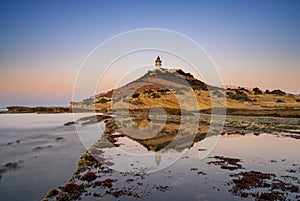 view of the Cabo de la Huerta lighthouse at sunrise with reflections in tidal pools in the foreground