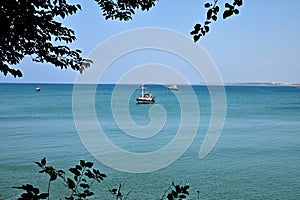 View of the calm blue sea from the shore. Yachts and boats are at anchor
