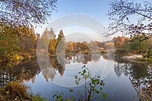 view of a calm river, autumn, Sunny day. In the foreground are beautiful twigs and leaves. Reflection